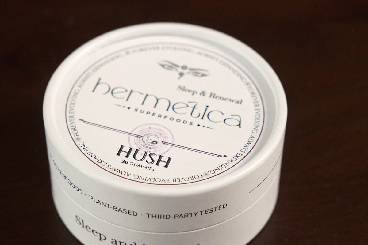 Jar of Hush sleep gummies on a nightstand beside a dim lamp and an open book at bedtime