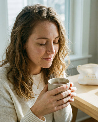 Woman enjoying a warm cup of Cozy adaptogenic chai latte in soft morning light