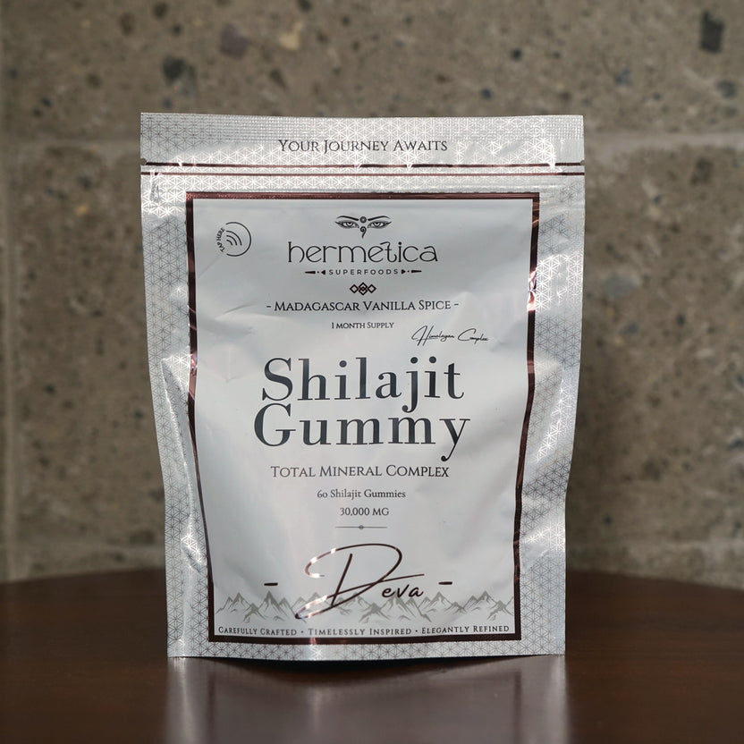 Deva Shilajit Gummies pouch on a walnut desk beside water and a linen notebook