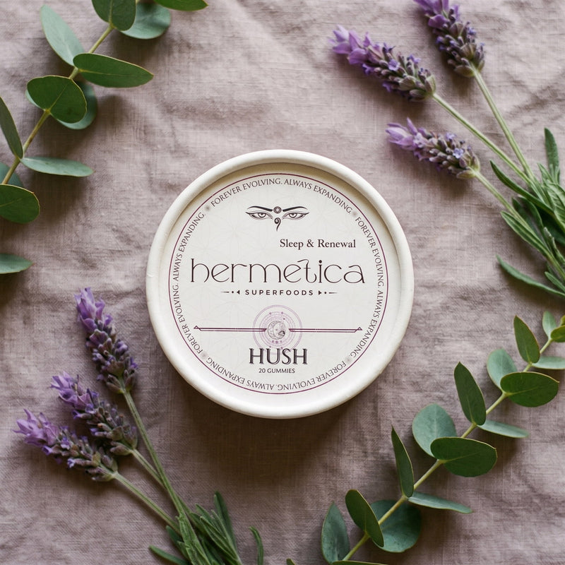 Overhead flat lay of the Hush Sleep Gummies tin on soft grey linen with lavender and eucalyptus