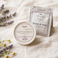 Hush Sleep Gummies tin resting on folded linen at the foot of a bed in soft morning light