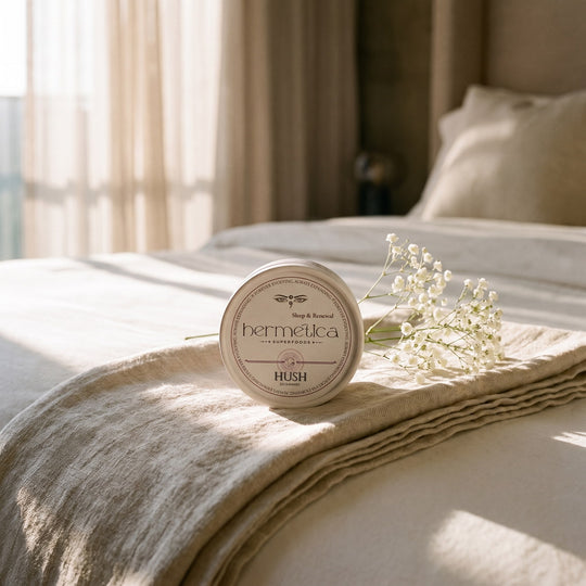 Hush Sleep Gummies tin resting on folded linen at the foot of a bed in soft morning light