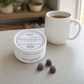 Hush Sleep Gummies tin resting on folded linen at the foot of a bed in soft morning light