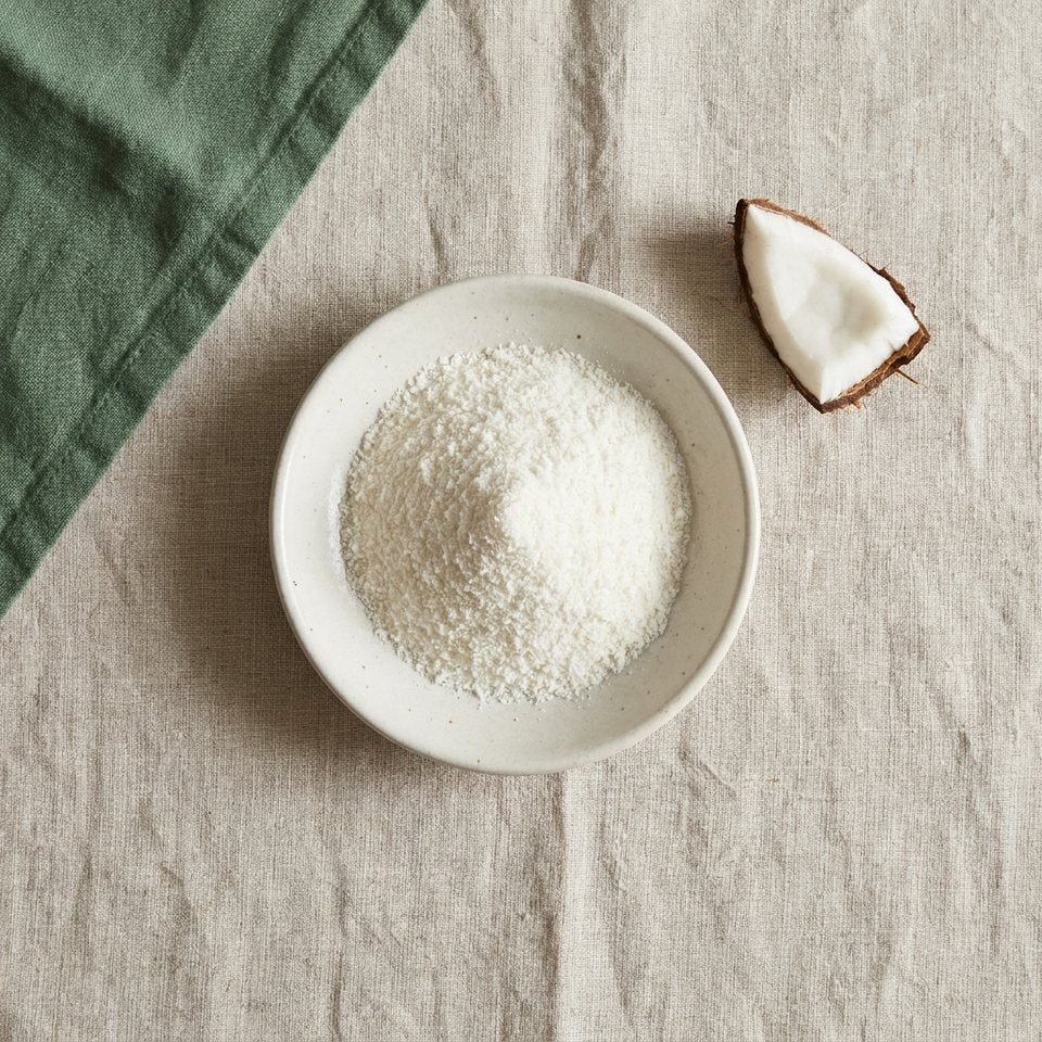 MCT oil powder in a small dish beside a piece of coconut